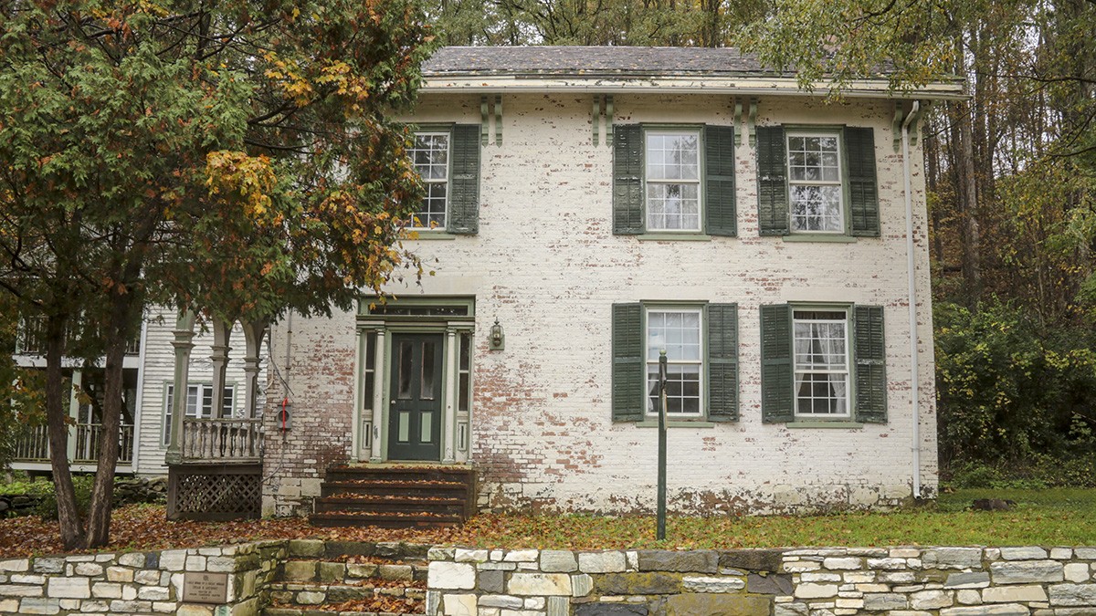 The Susan B. Anthony childhood home, a white brick house in Battenville, New York, with a VOTE sign in the front yard