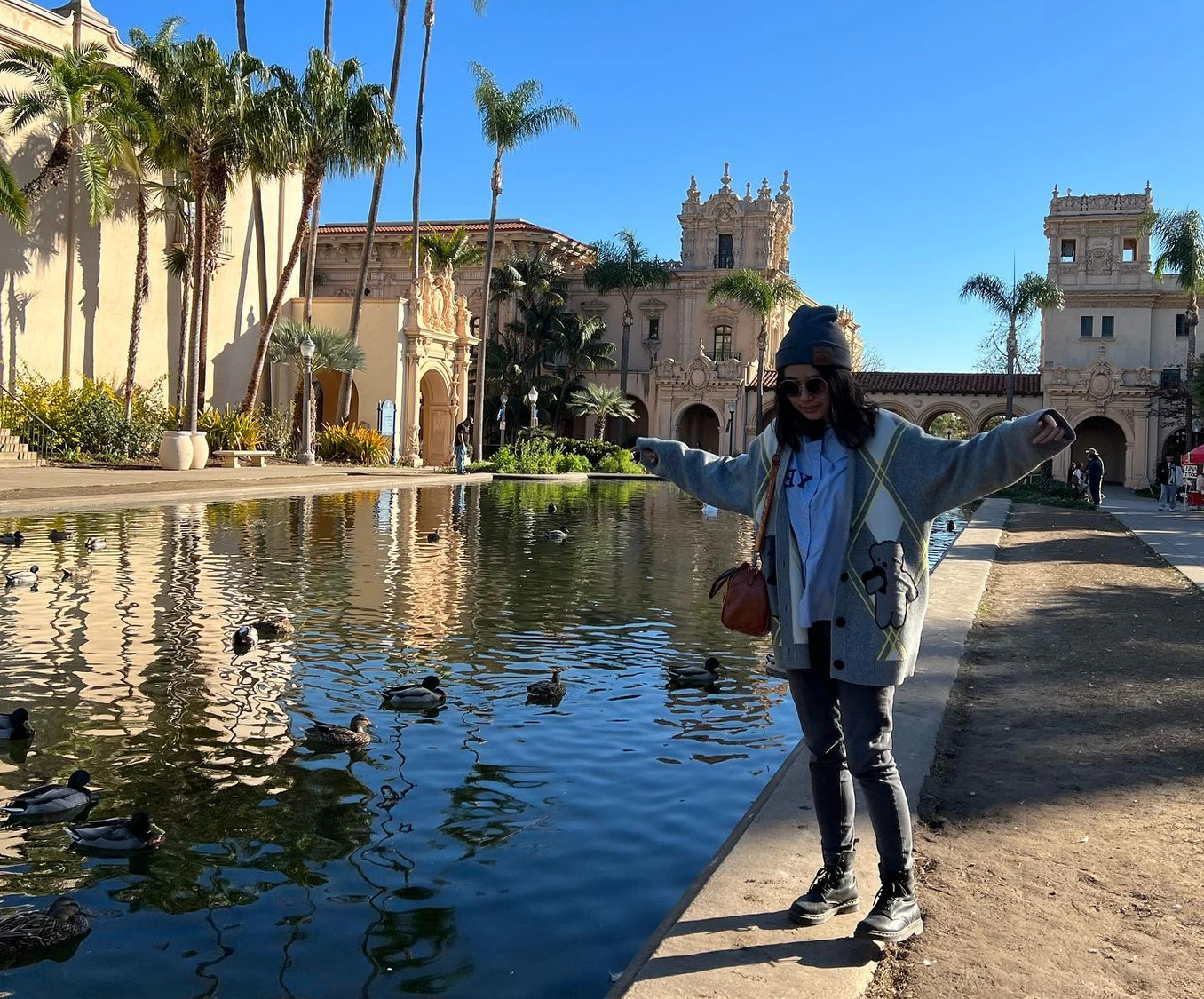 Stanlyn Lu standing by the reflecting pool at Balboa Park, arms outstretched.