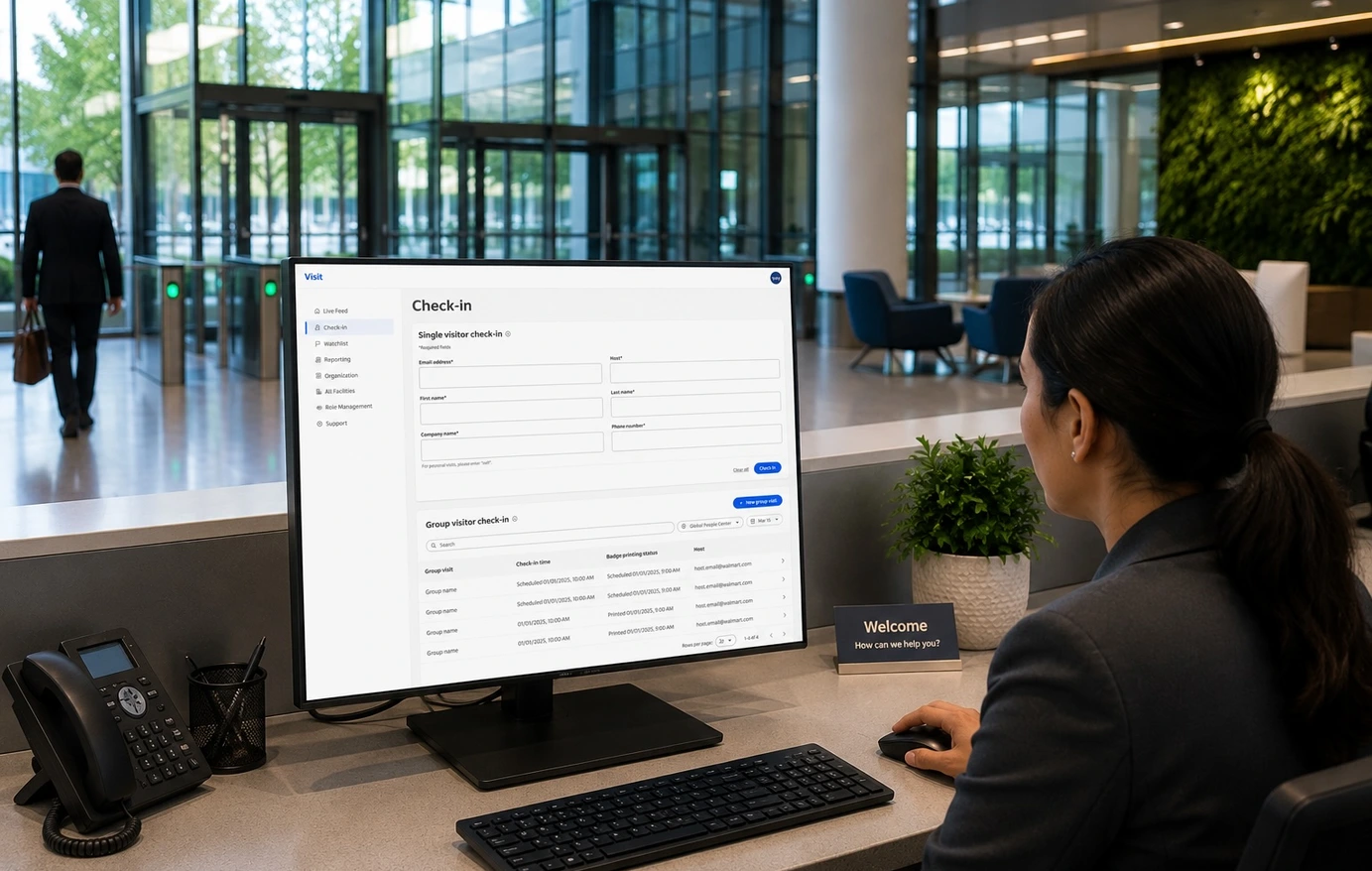 A reception desk monitor showing the visitor check-in admin form being completed by a front-desk associate.